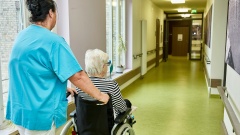 Pflegekraft mit einer Bewohnerin im Rollstuhl auf dem Flur in einem Pflegeheim