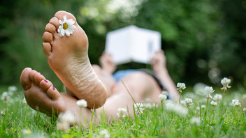 Frau mit Blume im Fuß liegt lesend im Gras