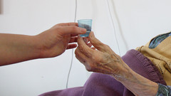 Pflegerin reicht alter Patientin Becher mit Wasser