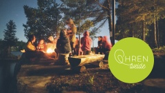 Menschengruppe sitzt im Wald am See um ein Lagerfeuer