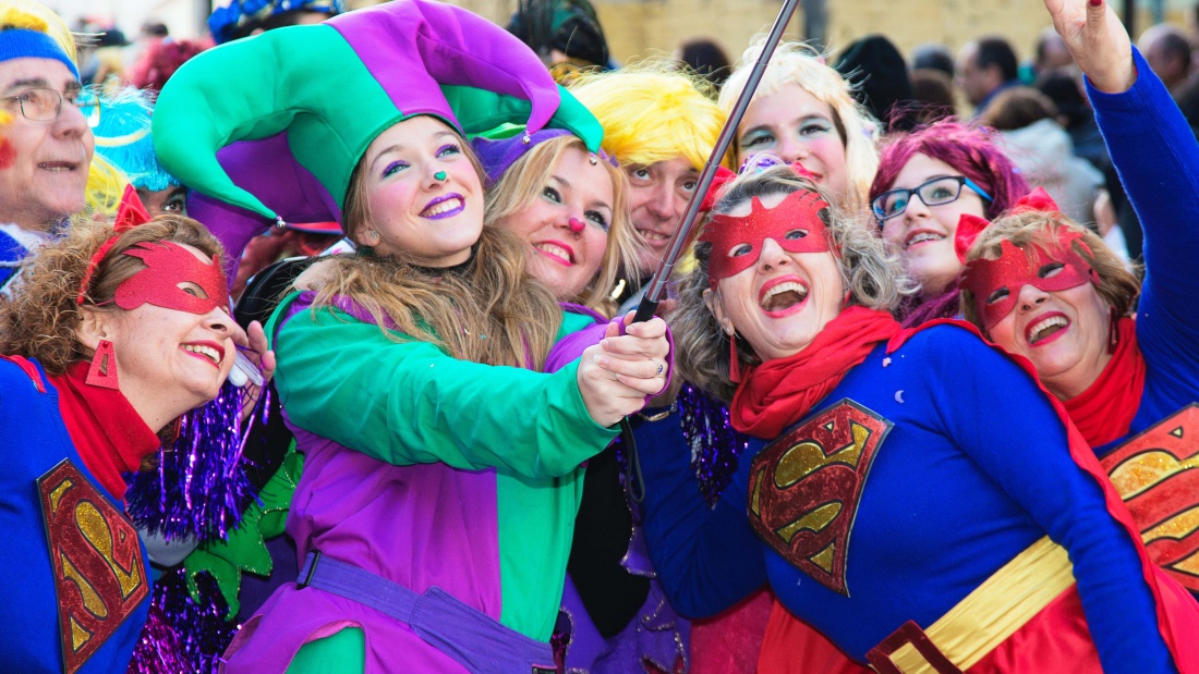 Ein Gruppe von bunt verkleideten lachenden Menschen posieren vor einem Selfie. 