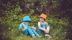 zwei Kinder mit Hüten und Büchern im Gras