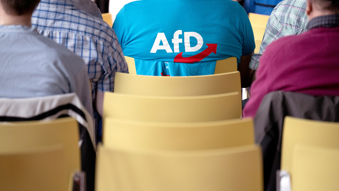 Ein Mann mit einem T-Shirt mit AfD-Logo sitzt in einer Stuhlreihe